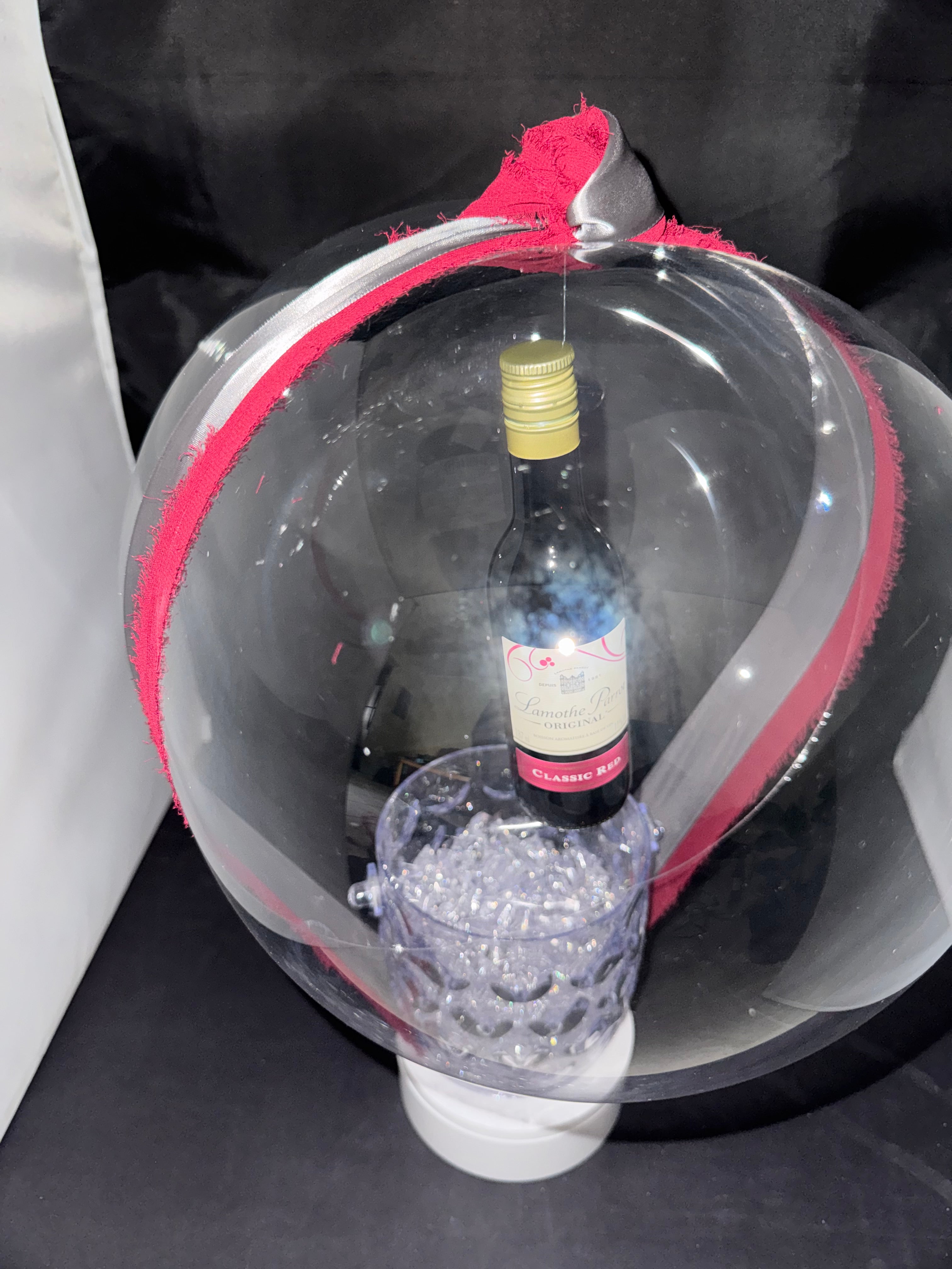 The Signature Luxe Bottle Bubble. This elegant gift turns  your bottles of choice into a stunning floating centerpieces. Ribbons of various colors gather at the top in a delicate bow, adding a graceful touch.