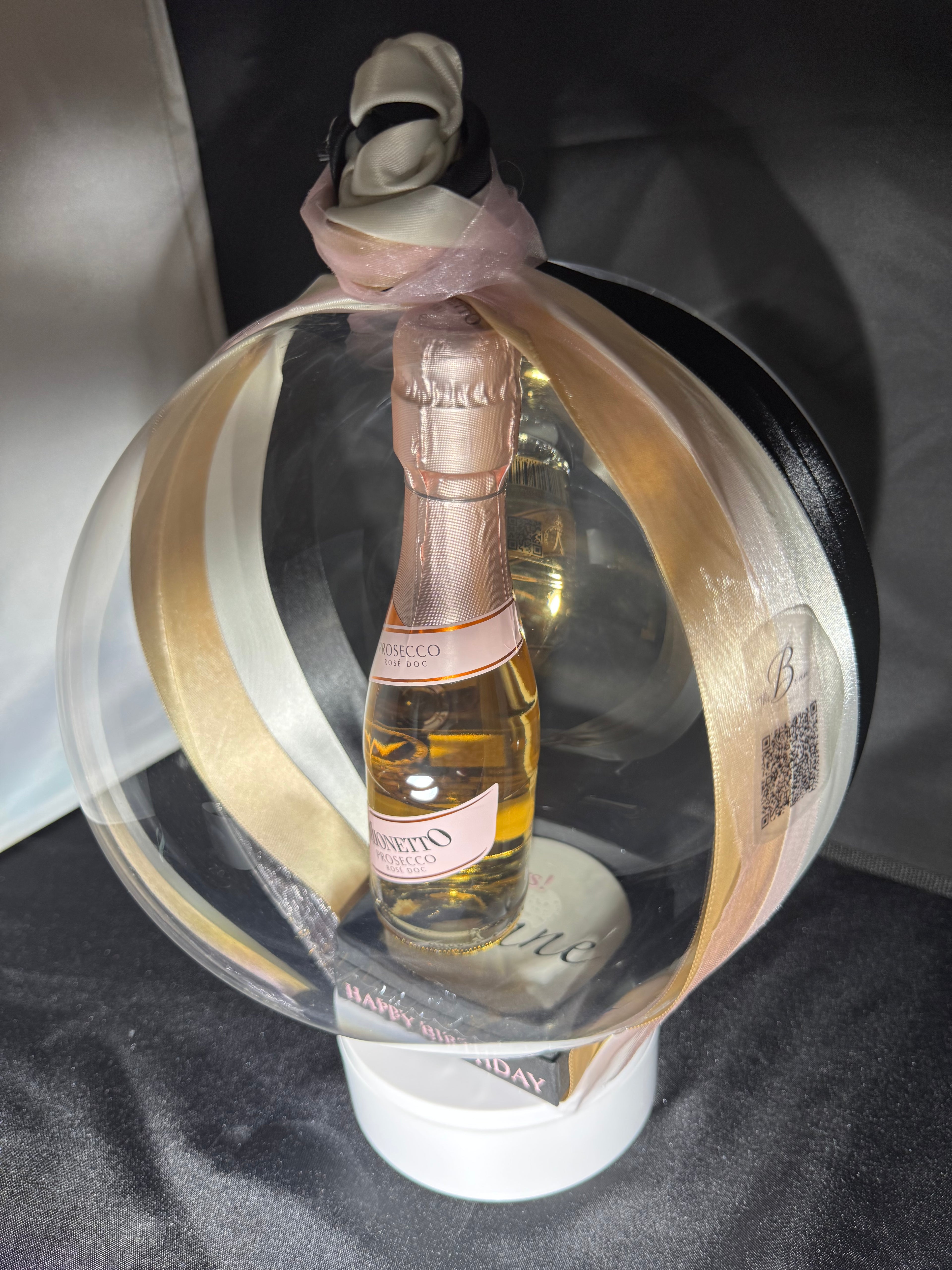 The Signature Luxe Bottle Bubble. This elegant gift turns  your bottles of choice into a stunning floating centerpieces. Ribbons of various colors gather at the top in a delicate bow, adding a graceful touch.