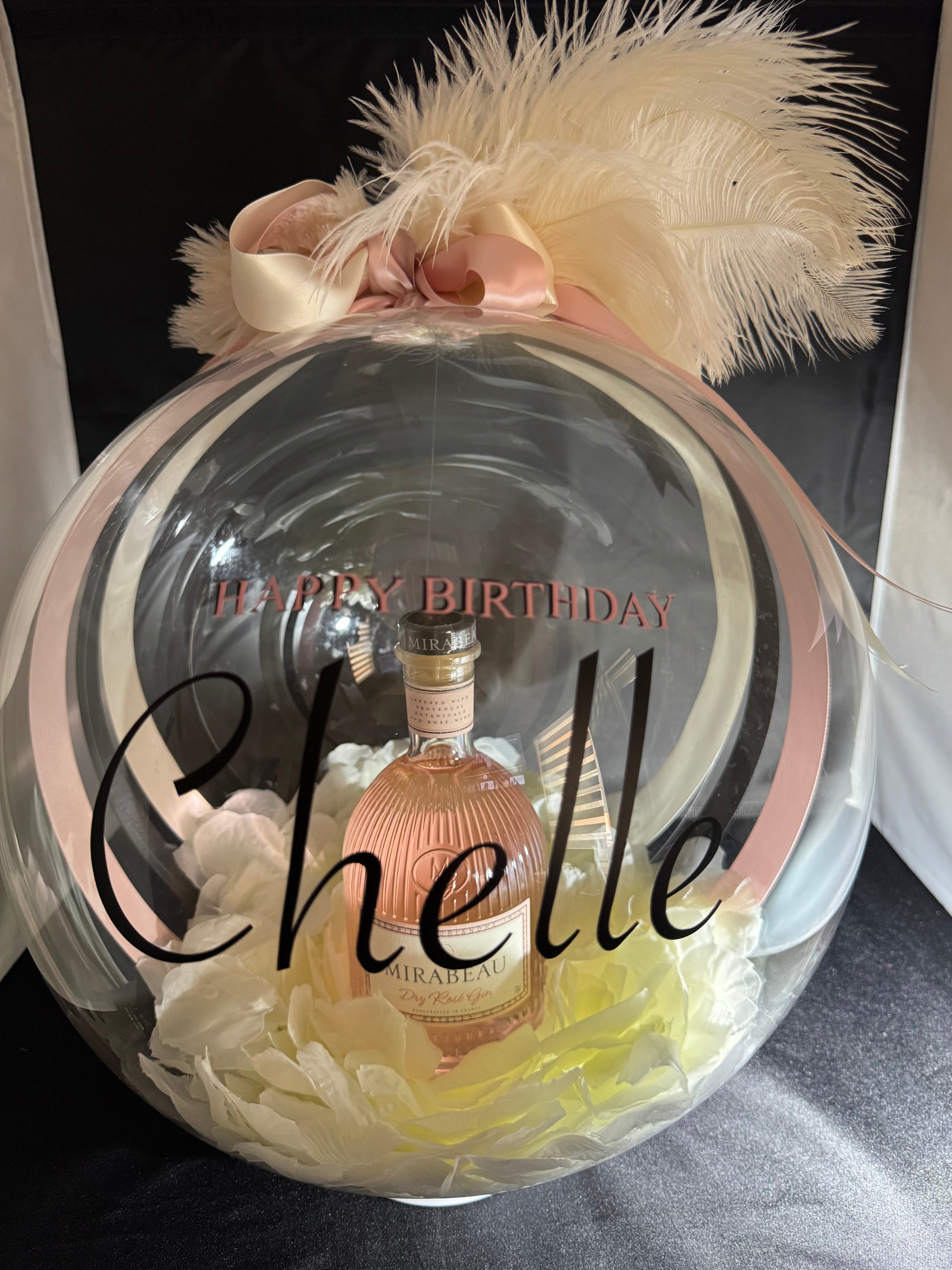 The Signature Luxe Bottle Bubble. This elegant gift turns  your bottles of choice into a stunning floating centerpieces. Ribbons of various colors gather at the top in a delicate bow, adding a graceful touch.