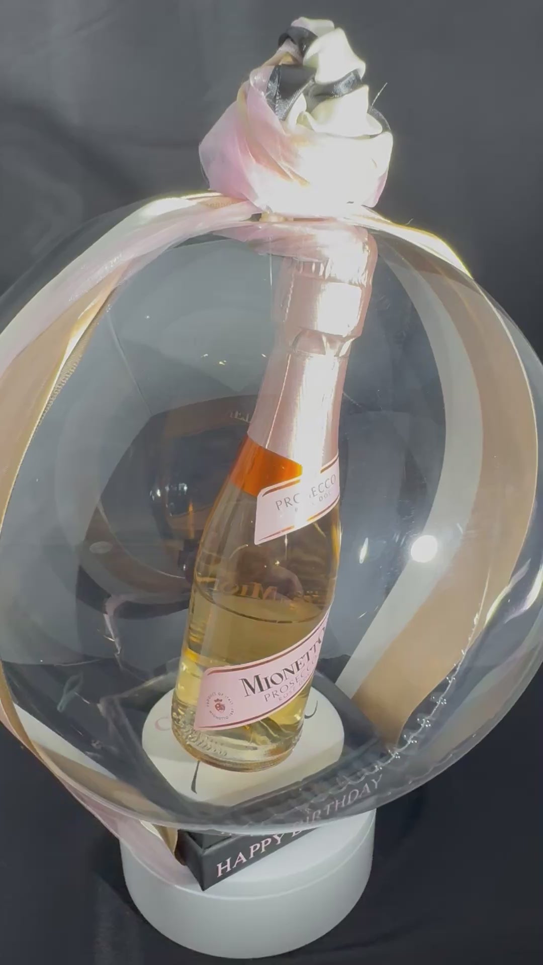 The Signature Luxe Bottle Bubble. This elegant gift turns  your bottles of choice into a stunning floating centerpieces. Ribbons of various colors gather at the top in a delicate bow, adding a graceful touch.
